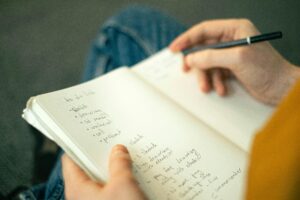 Close-up of a person taking notes in a notebook, writing a to-do list with a pencil.